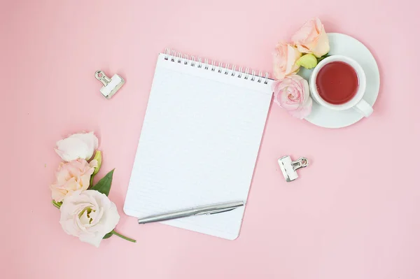 Kadınsı office çalışma alanı. Defter ile boşaltmak. Düz yatıyordu, sosyal medya, üstten görünüm. Pembe çiçekler, pastel pembe bir arka plan üzerinde çay.