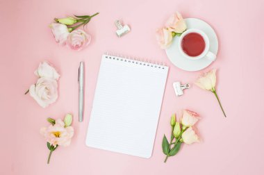 Kadınsı office çalışma alanı. Defter ile boşaltmak. Düz yatıyordu, sosyal medya, üstten görünüm. Pembe çiçekler, pastel pembe bir arka plan üzerinde çay.