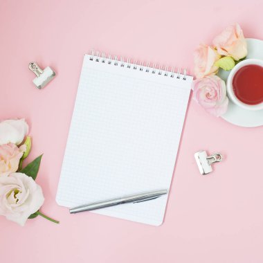 Kadınsı office çalışma alanı. Defter ile boşaltmak. Düz yatıyordu, sosyal medya, üstten görünüm. Pembe çiçekler, pastel pembe bir arka plan üzerinde çay.