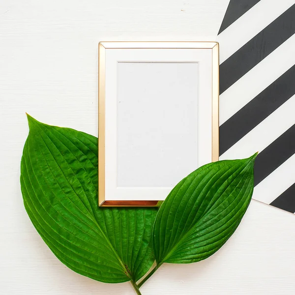 Gold photo frame with tropical leaves on black and white striped background. Mock up frame with copyspace. Flat lay, top view.