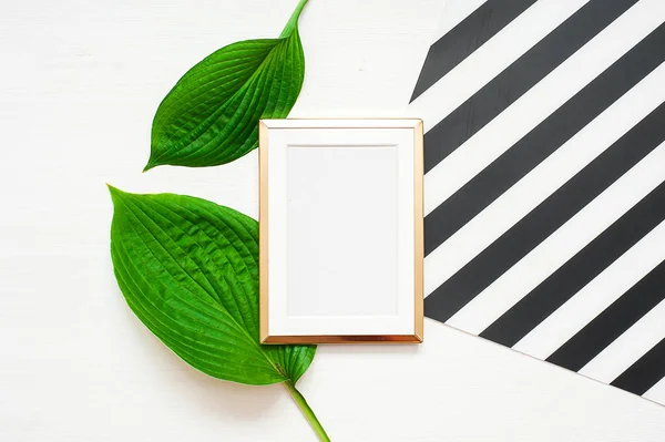 Gold photo frame with tropical leaves on black and white striped background. Mock up frame with copyspace. Flat lay, top view.
