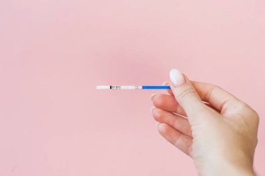 Hamilelik testi pembe bir arka plan üzerinde kadın elinde. Olumlu sonuç. 