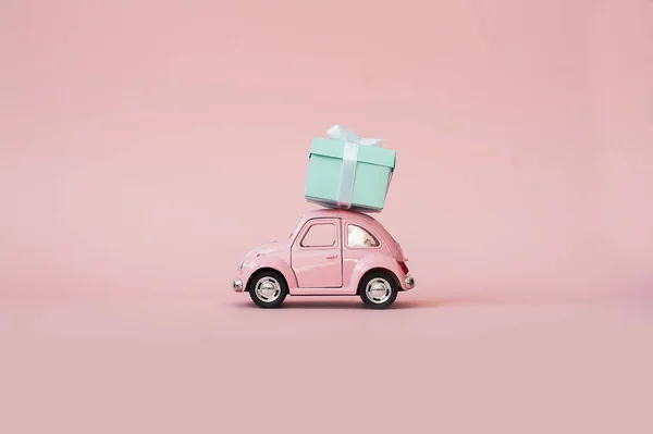 Pink toy  retro model car delivering gift box for Valentine's day on pink background. Volkswagen Beetle on pink background.