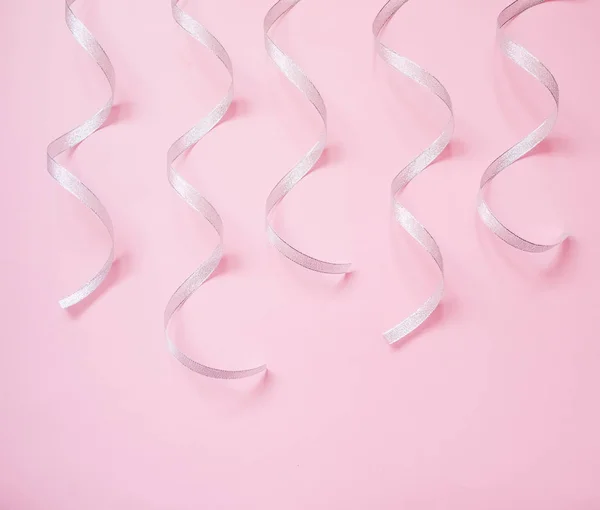 Silver streamers serpentine on pastel pink background. Christmas gift. Concept for celebration, carnival, party, festive sales. — Stock Photo, Image