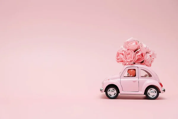 Pink retro toy car delivering bouquet of flowers box on pink background. February 14 card for Valentine's day. Flower delivery. 8 March, International Happy Women's Day. — Stock Photo, Image