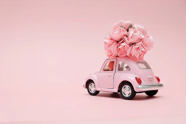 Pink retro toy car delivering bouquet of flowers box on pink background. February 14 card for Valentine's day. Flower delivery. 8 March, International Happy Women's Day. — Stock Photo, Image