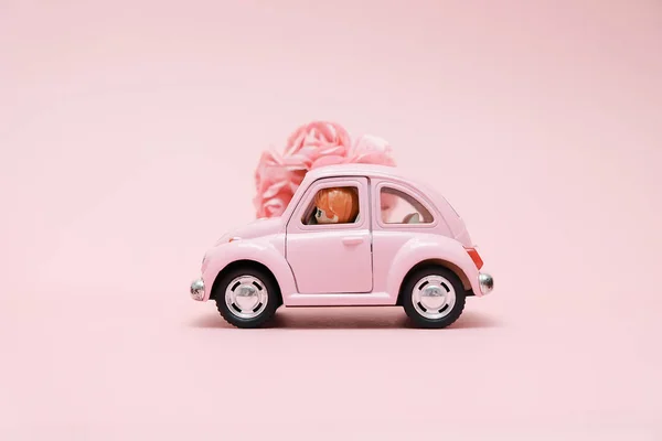 Pink retro toy car delivering bouquet of flowers box on pink background. February 14 card for Valentine\'s day. Flower delivery. 8 March, International Happy Women\'s Day