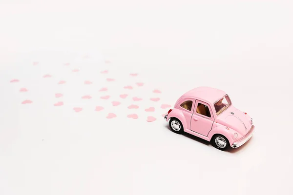 Rosa coche de juguete retro entrega corazones caja sobre fondo rosa. Tarjeta del 14 de febrero para el día de San Valentín. Entrega de flores. 8 de marzo, Día Internacional de la Mujer . —  Fotos de Stock