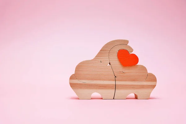 Bonitas figuras de elefante de madeira segurando o coração em fundo rosa. Produtos feitos à mão. O conceito do dia dos namorados . — Fotografia de Stock