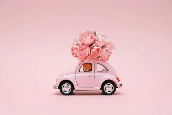 Pink retro toy car delivering bouquet of flowers box on pink background. February 14 card for Valentine\'s day. Flower delivery. 8 March, International Happy Women\'s Day.
