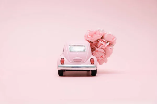 Rosa Retro-Spielzeugauto liefert Blumenstrauß Box auf rosa Hintergrund. 14. Februar Karte für den Valentinstag. Blumenlieferung. 8. März, internationaler fröhlicher Frauentag. — Stockfoto