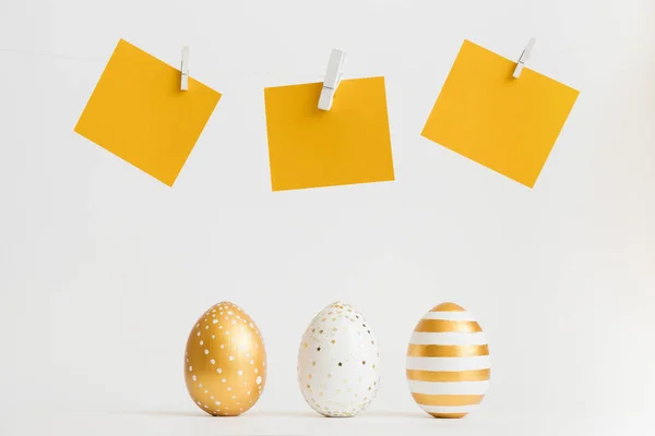 Beyaz arka plan üzerinde üstlerindeki sarı metin etiketleri ile üst üste üç dekore edilmiş altın yumurta hazır. En az Paskalya kavramı — Stok fotoğraf