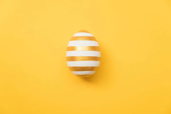 Ostern golden mit gestreiftem gemustertem Ei auf gelbem Hintergrund. Minimales Osterkonzept. frohe Osterkarte mit Kopierplatz für Text. — Stockfoto