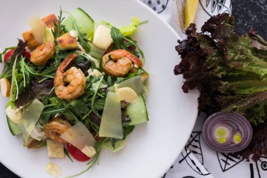 Karanlık taş zemin üzerine beyaz bir tabak karides ile taze Sezar salatası. İngridients aşçı için düz yatırın.