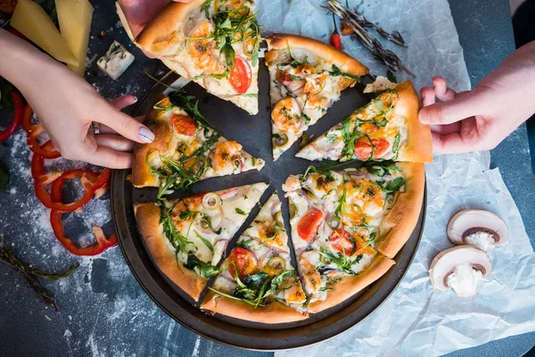 Friends eating pizza. People\'s hands grabbing a slice of pizza