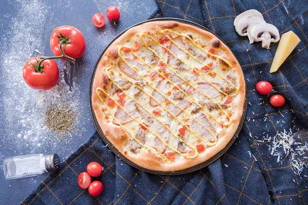 Piatto con pizza tradizionale italiana con chiken, prosciutto, pepe, formaggio e pomodori sulla tavola di pietra blu scuro e ingredienti — Foto Stock