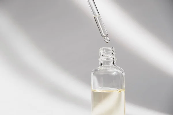Dropper glass Bottle Mock-Up. Oily drop falls from cosmetic pipette on white background