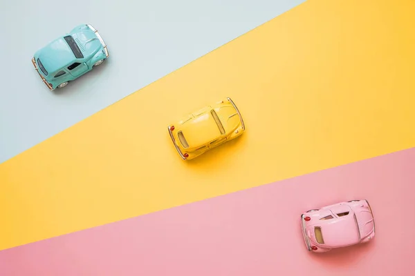 Small color toy cars on a yellow, pink and blue background. Raci