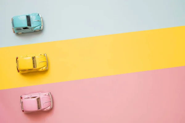 Small color toy cars at the start on a yellow, pink and blue bac