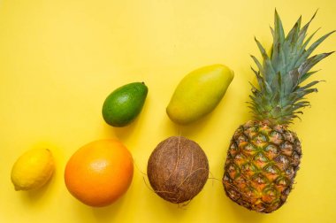 Düz sarı arka plan üzerinde tropikal meyve seti ile yatıyordu. Yaz taze gıda: hindistan cevizi, ananas, mango, greyfurt, limon, avokado. Vegan.