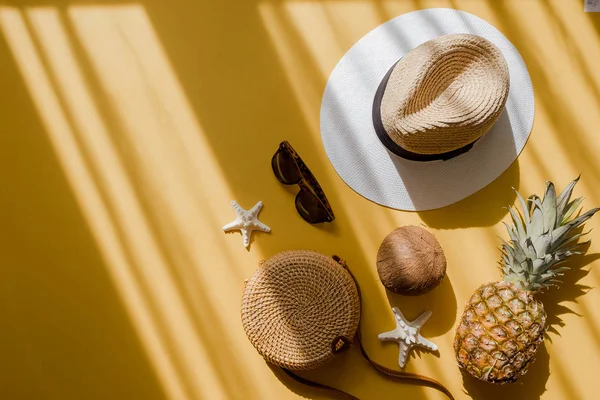 Colorful summer female fashion outfit flat lay. Straw hat, bamboo bag, sunglasses, coconut, pineapple over yellow background — Stock Photo, Image