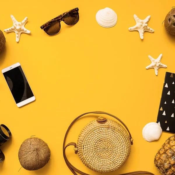 Summer traveler accessories flat lay. Straw hat, camera, bag, sunglasses, coconut, pineapple, plane, notebook and phone on yellow