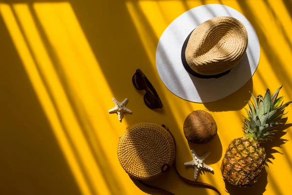 Colorful summer female fashion outfit flat lay. Straw hat, bamboo bag, sunglasses, coconut, pineapple, starfish over yellow background, top view. Summer fashion, holiday concept — Stock Photo, Image