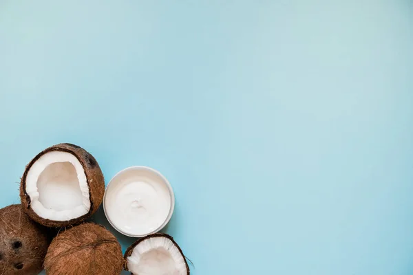 Otwarty szklany słoik ze świeżym olejem kokosowym i dojrzałych kokosów na niebieskim tle. — Zdjęcie stockowe