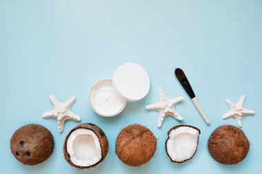 Mavi arka plan üzerinde taze hindistan cevizi yağı ve olgun hindistan cevizi ile açılan cam kavanoz. Ev yapımı hindistan cevizi ürünleri