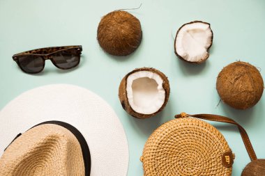 Düz mavi arka plan üzerinde olgun hindistan cevizi ile yatıyordu. Güneş gözlüğü, hasır şapka, bambu çanta ile Yaratıcı yaz düzeni.