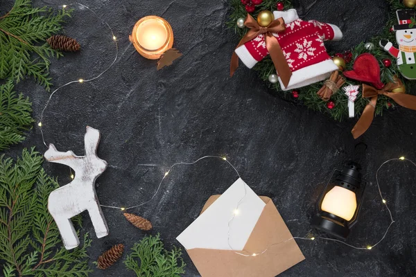 Christmas composition. Gifts, envelope, fir tree branches, white decorations on black background.