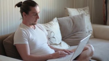 Genç serbest çalışan öğrenci dizüstü bilgisayarını kullanıyor internette çalışıyor, milenyum adamı gülümsüyor bilgisayar sörfü internetinde daktilo yazıyor ve uzaktaki işinden zevk alıyor.