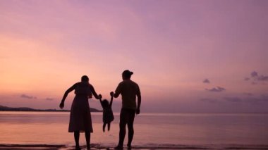 Üç kişilik aile gün batımında tropik plajda oynuyorlar. Mutlu aile kavramı.