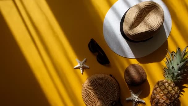 Πολύχρωμο καλοκαίρι γυναικεία μόδα στολή επίπεδη θέσει. Ψάθινο καπέλο, τσάντα μπαμπού, γυαλιά ηλίου, καρύδα, ανανάς, αστερίας πάνω από κίτρινο φόντο, πάνω όψη. Καλοκαιρινή μόδα, διακοπές έννοια. — Αρχείο Βίντεο