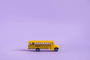 Okul konseptine geri dönelim. Mor arka planda geleneksel sarı okul otobüsü. Okula nakil ol. Sarı oyuncak model okul otobüsü.