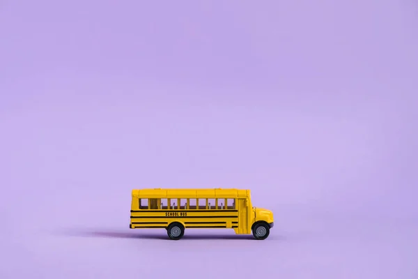 Back to school concept. Traditional yellow school bus on purple background. Transfer to school. Yellow toy model school bus.