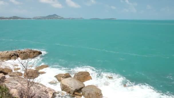 Kraftfulla vågor och stänk bryter på en stenig strand med havsskum. Blå azurblå havsvatten, havsstrand, stenkust. — Stockvideo