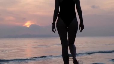 Mutlu Kaygısız Kadın Sahilde Güzel Günbatımının tadını çıkarıyor. Gün batımında suya girip ufku terk eden bir kızın silueti..