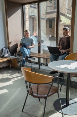 In a bright and modern office space, two men are actively collaborating on their laptops, exchanging fresh ideas