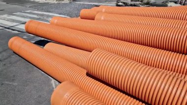 Kanalizasyon borusu, çift katmanlı. Borular üst üste yığılmış, şehirde tamirat yapılmış. Turuncu kanalizasyon boruları, yakın plan. Borular topraktan gelen değişken yüklere dayanabilir.