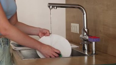 Bulaşıkları yıkayan kadın, elleri yakın çekim. Ev işleri işte. Kız lavabonun yanında duruyor ve bulaşıkları yıkıyor. Bulaşıkları yıkadıktan sonra, kız onu bir havlunun üzerine koyar. Ev hanımı mutfağı temizler.