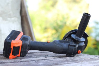 Kablosuz öğütücü yakın planda, ahşap bir yüzeye uzanıyor. Kulübede ya da inşaatta tamirat. Çalışan alet. Kablosuz kablosuz öğütücü. Elektrikli aletler. DIY tamir konsepti, inşaat ekipmanları