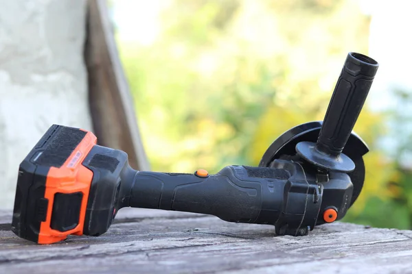 Kablosuz öğütücü yakın planda, ahşap bir yüzeye uzanıyor. Kulübede ya da inşaatta tamirat. Çalışan alet. Kablosuz kablosuz öğütücü. Elektrikli aletler. DIY tamir konsepti, inşaat ekipmanları