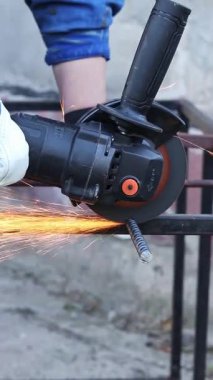 Close-up of an angle grinder cutting rebar. Female hands in work gloves holding a cordless grinder and cutting rebar into small pieces. Power tool for construction and repair work