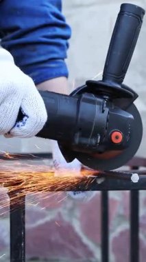 Close-up of an angle grinder cutting rebar. Female hands in work gloves holding a cordless grinder and cutting rebar into small pieces. Power tool for construction and repair work