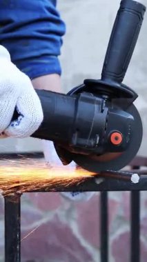 Close-up of an angle grinder cutting rebar. Female hands in work gloves holding a cordless grinder and cutting rebar into small pieces. Power tool for construction and repair work