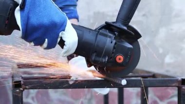 Close-up of an angle grinder cutting rebar. Female hands in work gloves holding a cordless grinder and cutting rebar into small pieces. Power tool for construction and repair work
