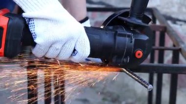 Close-up of an angle grinder cutting rebar. Female hands in work gloves holding a cordless grinder and cutting rebar into small pieces. Power tool for construction and repair work
