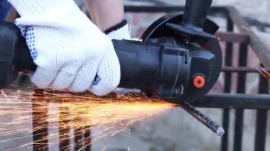 Close-up of an angle grinder cutting rebar. Female hands in work gloves holding a cordless grinder and cutting rebar into small pieces. Power tool for construction and repair work