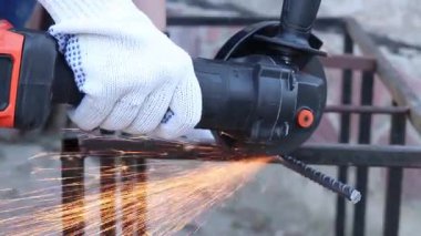 Close-up of an angle grinder cutting rebar. Female hands in work gloves holding a cordless grinder and cutting rebar into small pieces. Power tool for construction and repair work